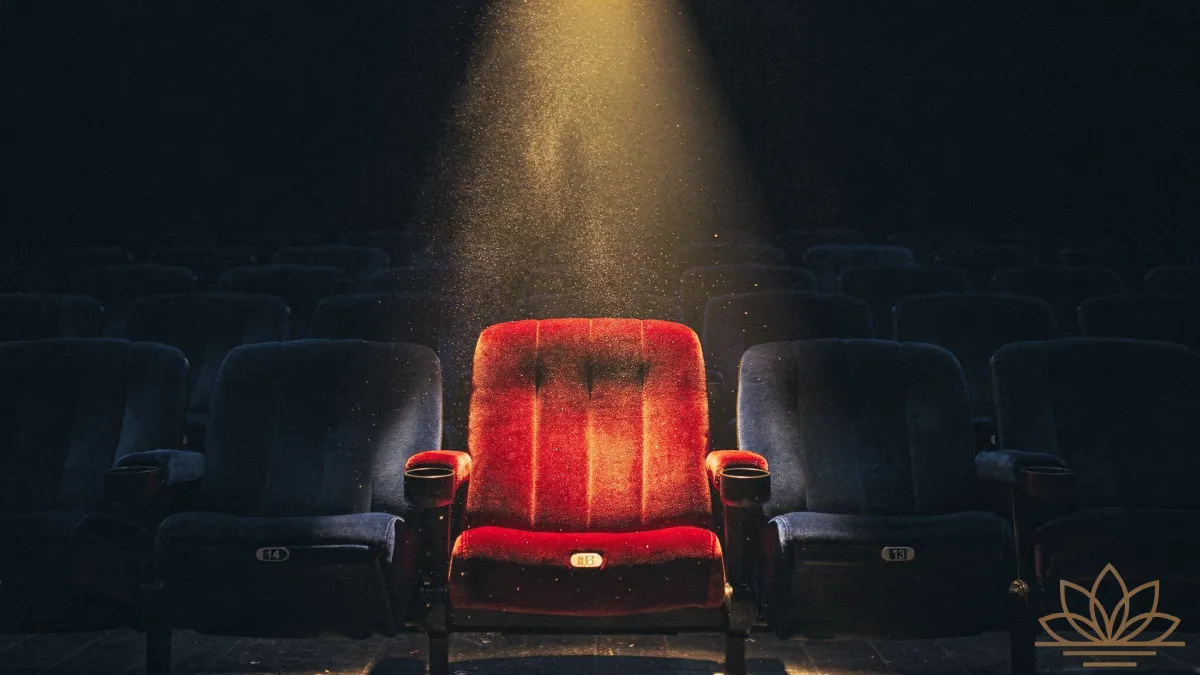 `A single empty theater seat lit by a warm spotlight in an otherwise dark cinema, LT Clinical lotus mark in the corner`
