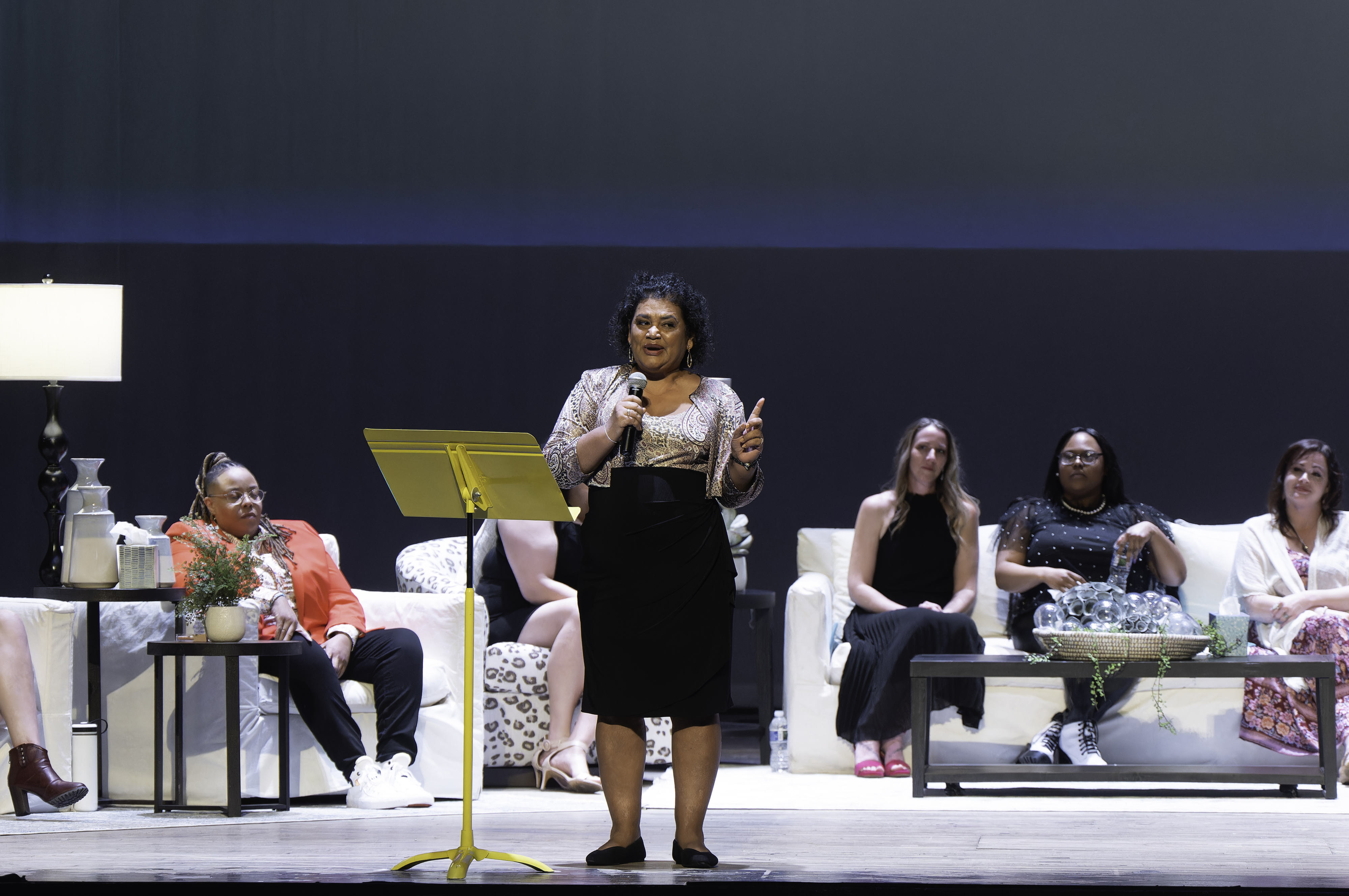 Image of a diverse group of women singing and dancing on stage with an audience in front of them