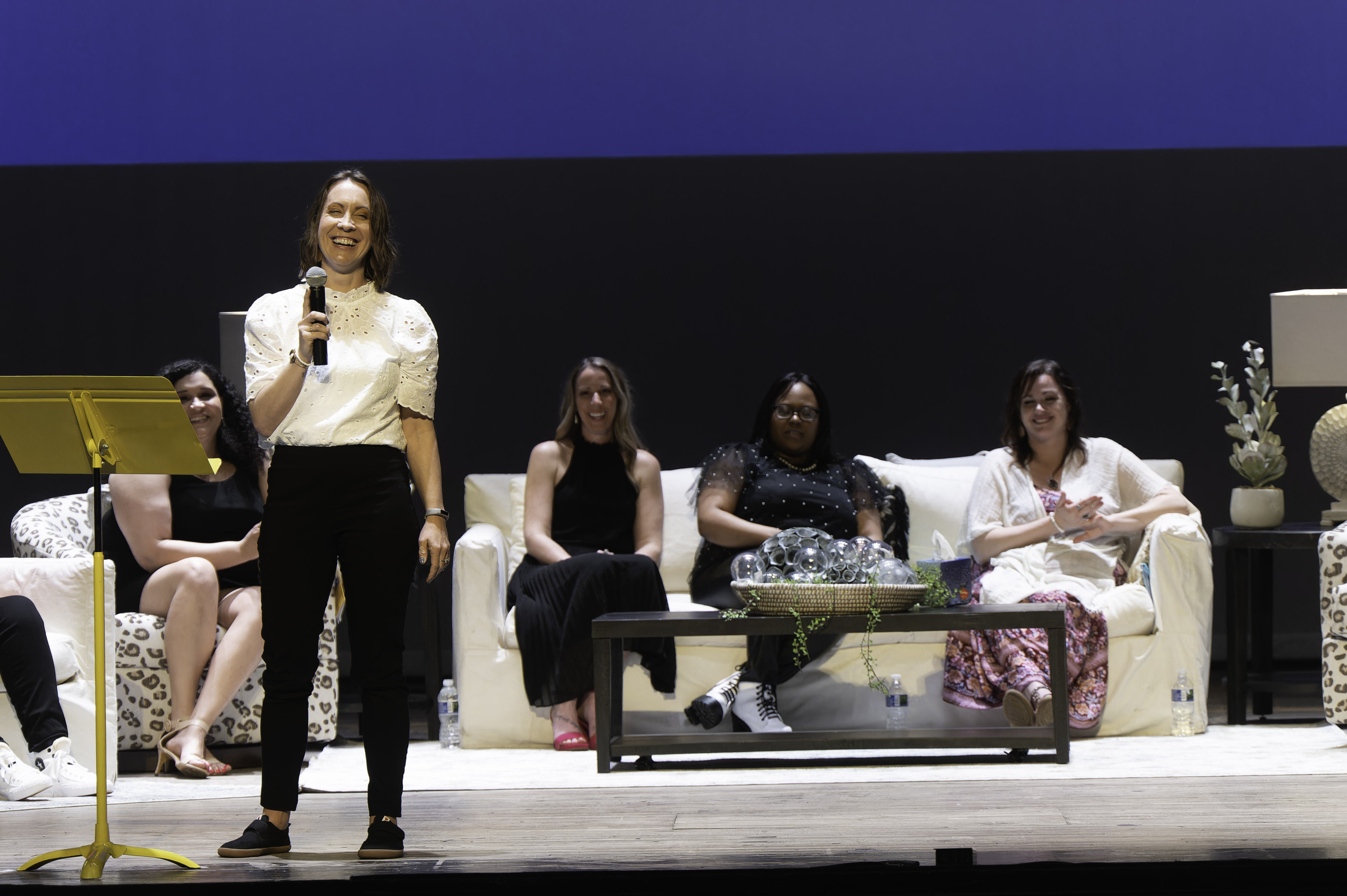 Image of a group of women singing and dancing on stage with an audience in front of them