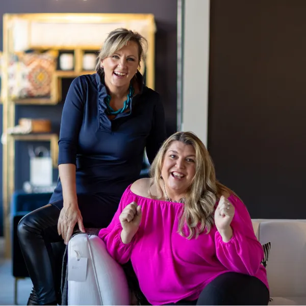 TWSS Founders Kerry Ross sitting on arm of a couch and Jenette Jurczyk sitting on the couch