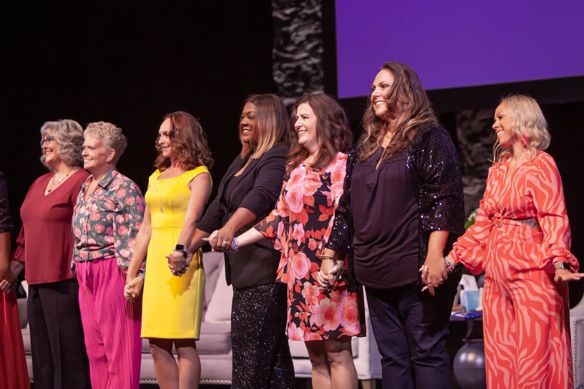 Image of a diverse group of women holding hands on-stage at a TWSS event
