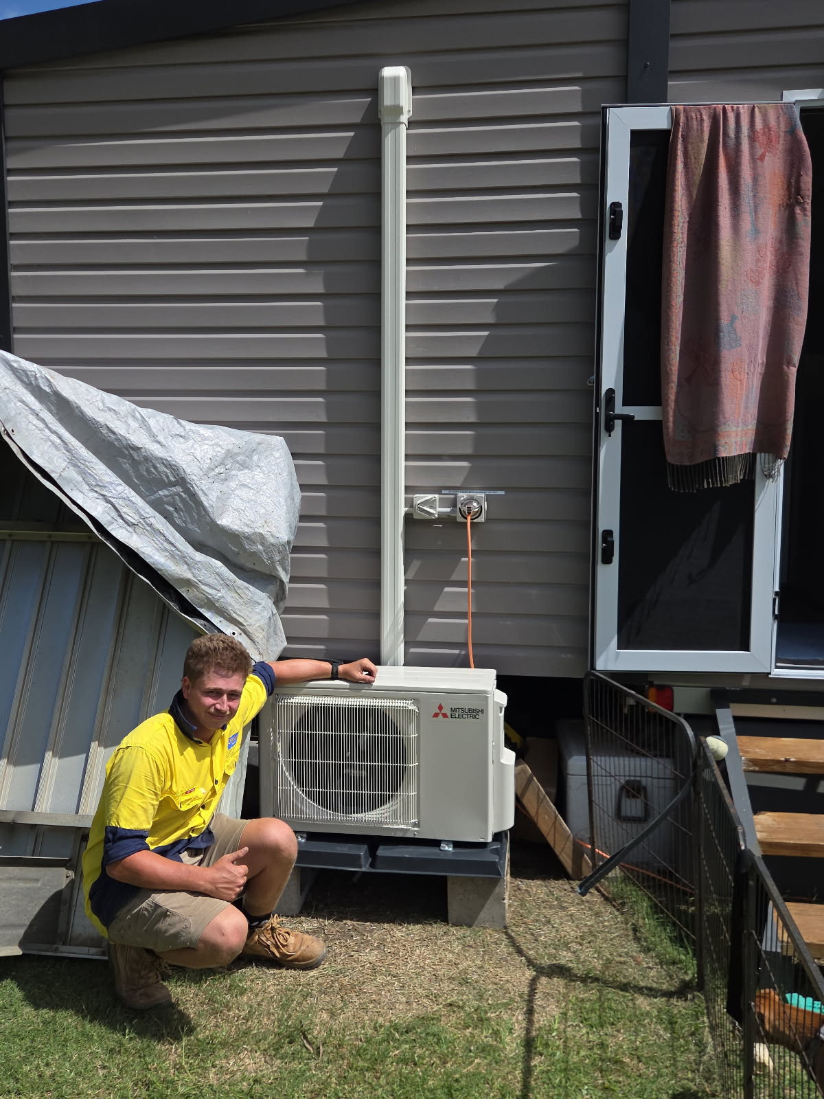 O'Brien technician beside a Mitsubishi outdoor air conditioning unit installed on stands beside a house