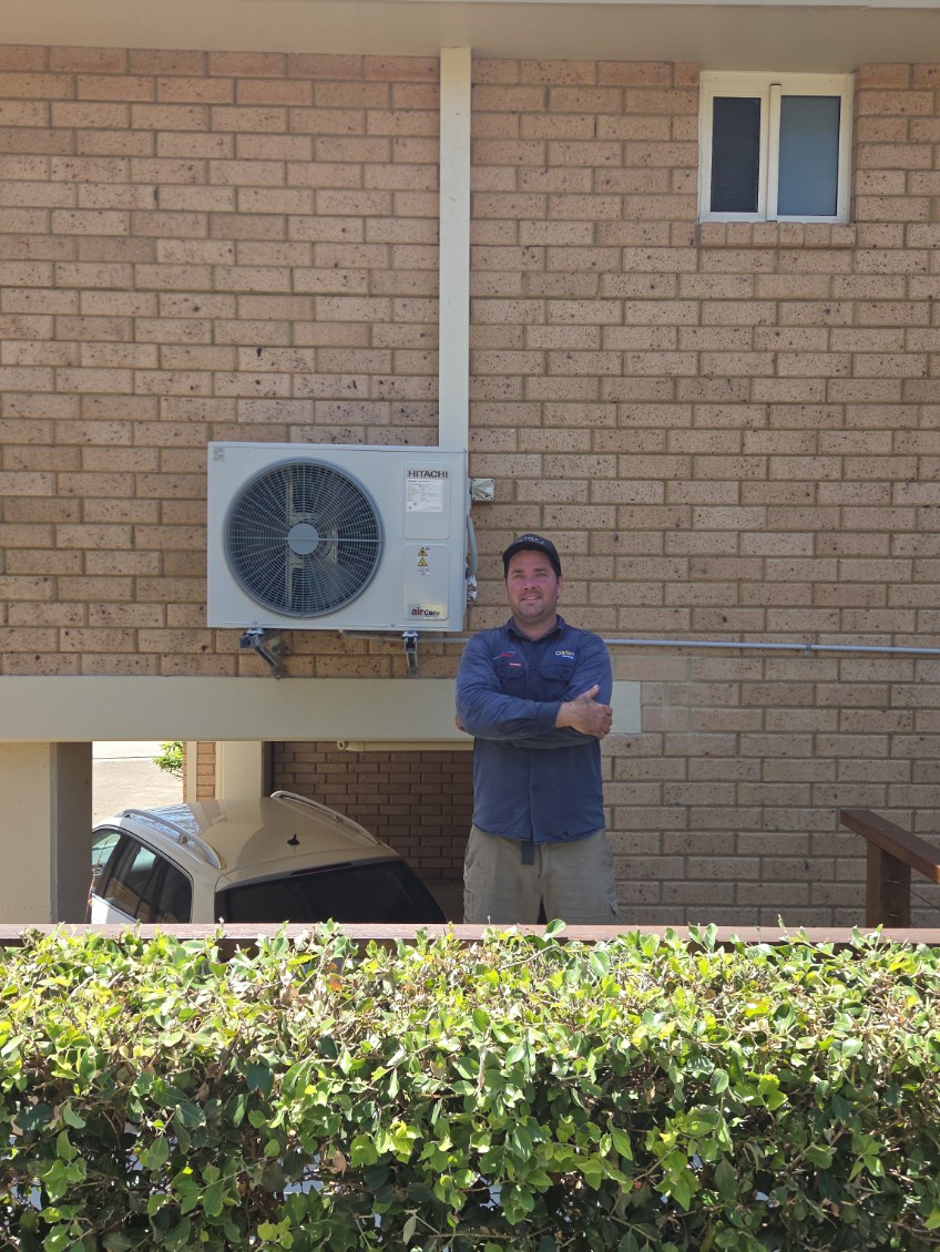 Hitachi outdoor air conditioning unit bracket-mounted on a brick wall above a carport