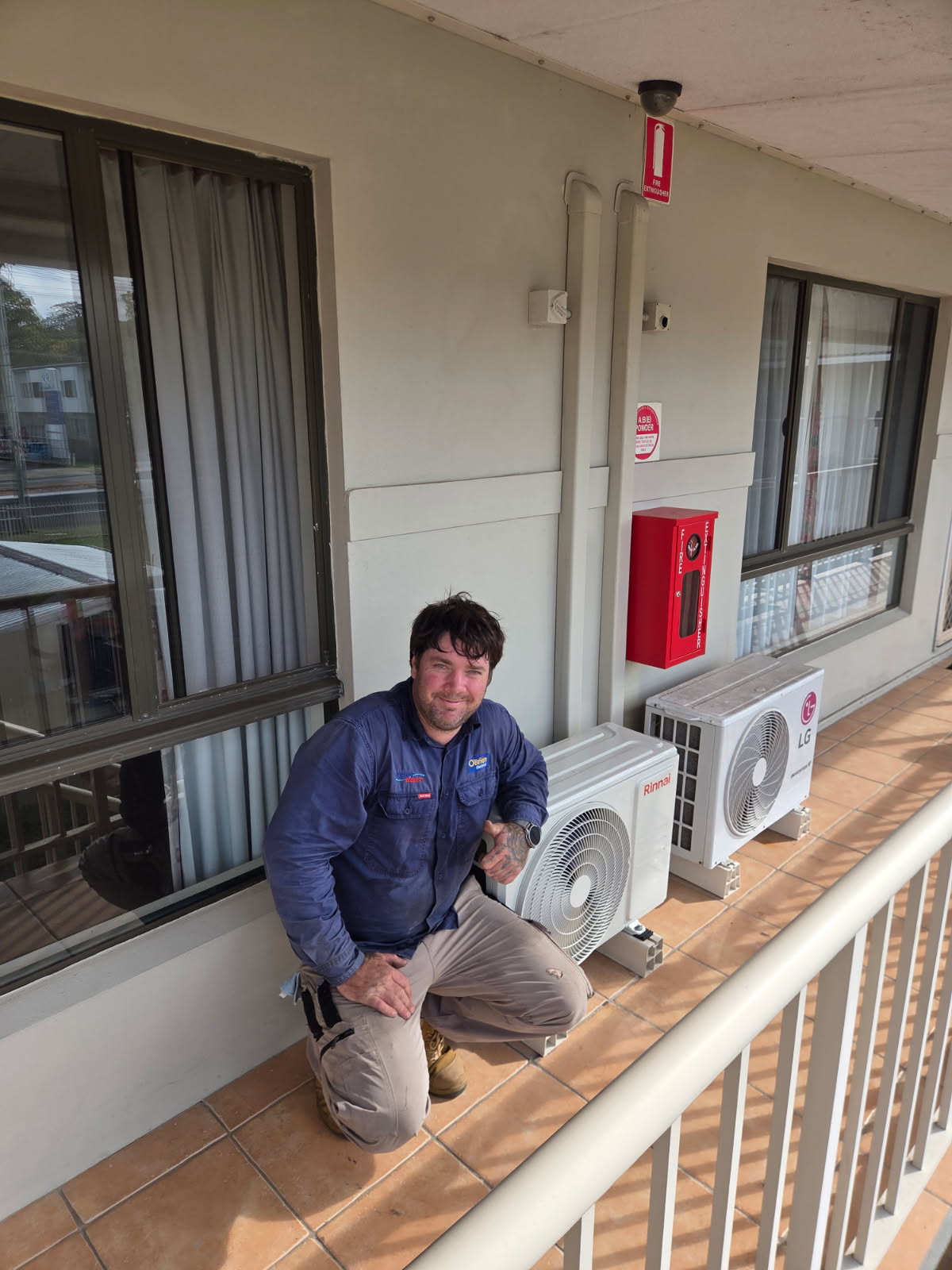 O'Brien technician beside two outdoor air conditioning units on a unit balcony