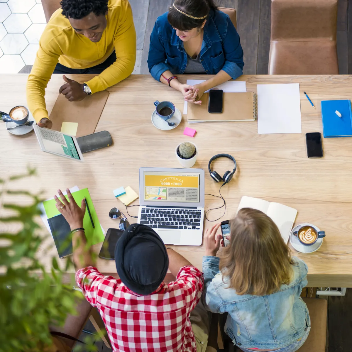 A diverse group of professionals collaborating around a large wooden table, laptops and coffee cups in view, brainstorming marketing strategies and sharing creative ideas in a relaxed workspace