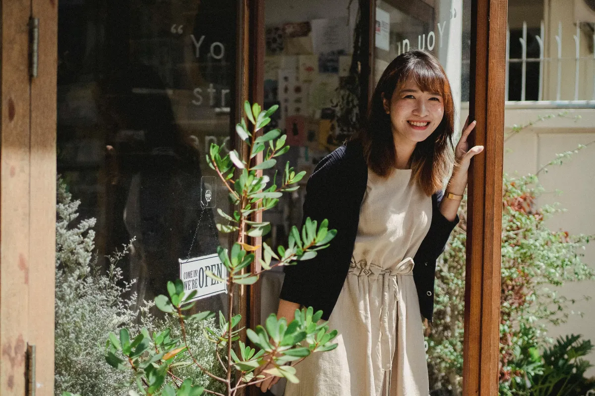 Smiling female shop owner standing in a doorway, illustrating how tailored marketing and operational strategies can boost growth.