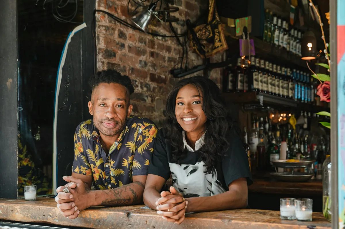 Two café owners smiling behind the counter, representing a thriving small business built on genuine customer engagement.