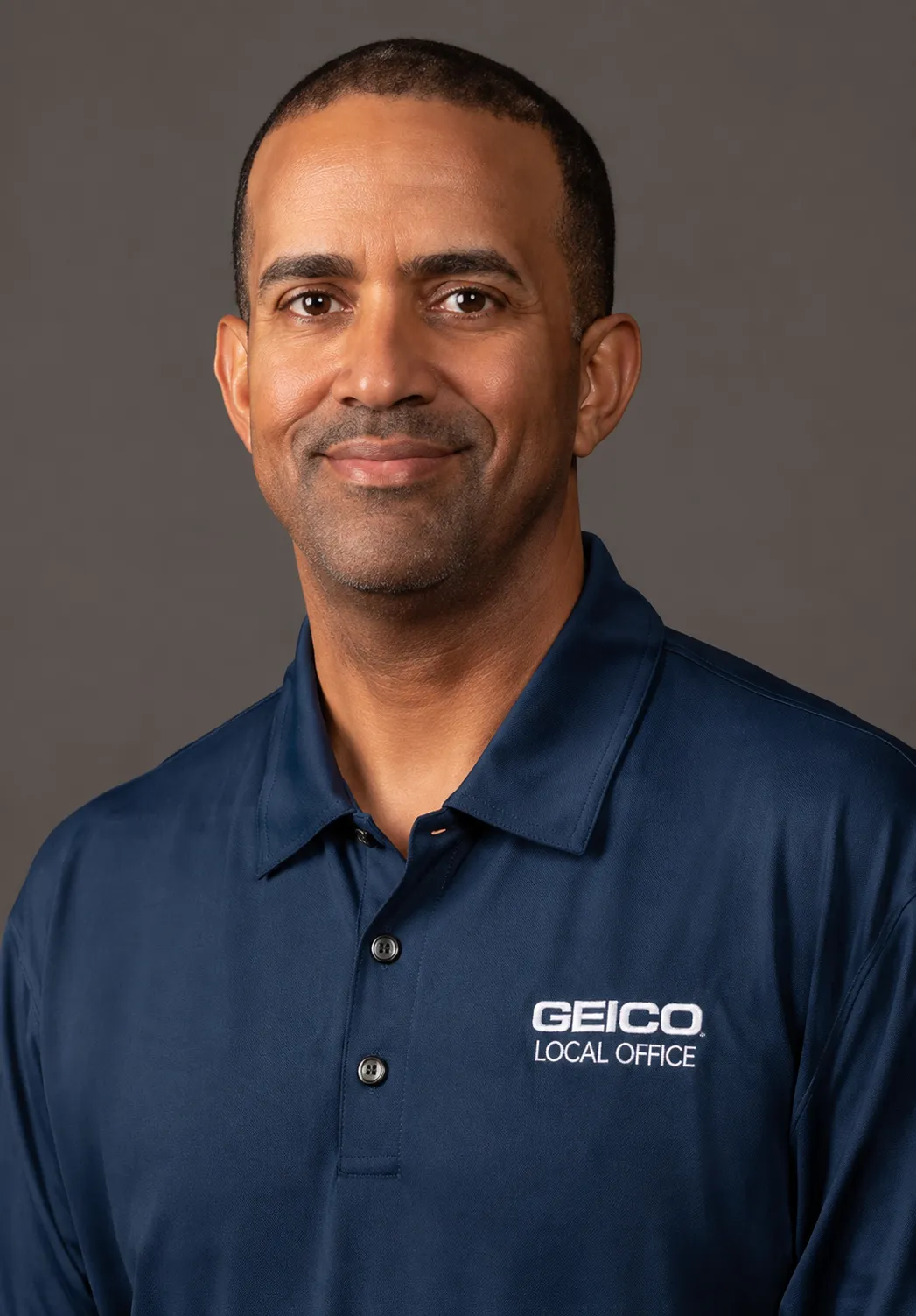 Circular portrait of a smiling woman with blonde hair wearing a blue polo shirt with a GEICO logo
