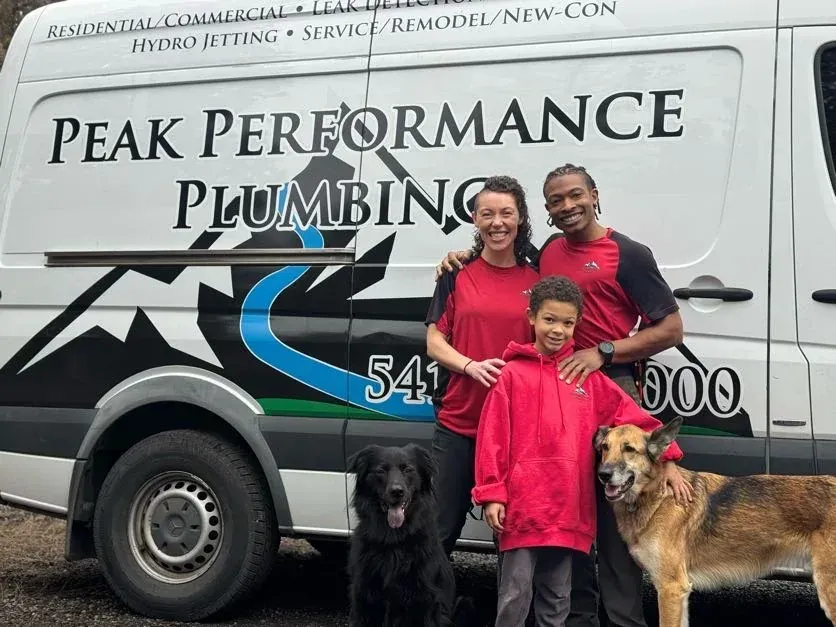 Donovan Jones, owner of Peak Performance Plumbing, with his family and dogs in front of a branded plumbing van in Bend Oregon
