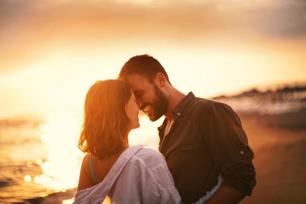 Romantic couple embracing at sunset on the beach, smiling and connecting emotionally, representing healthy relationships and intimacy