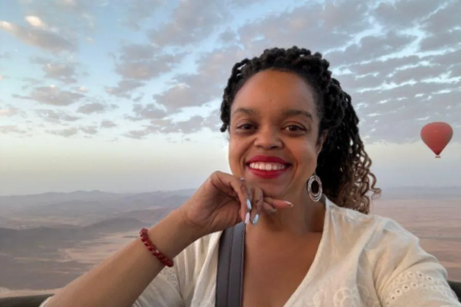 Jasmin Bryant smiling in a white blouse with a hot air balloon floating behind her.