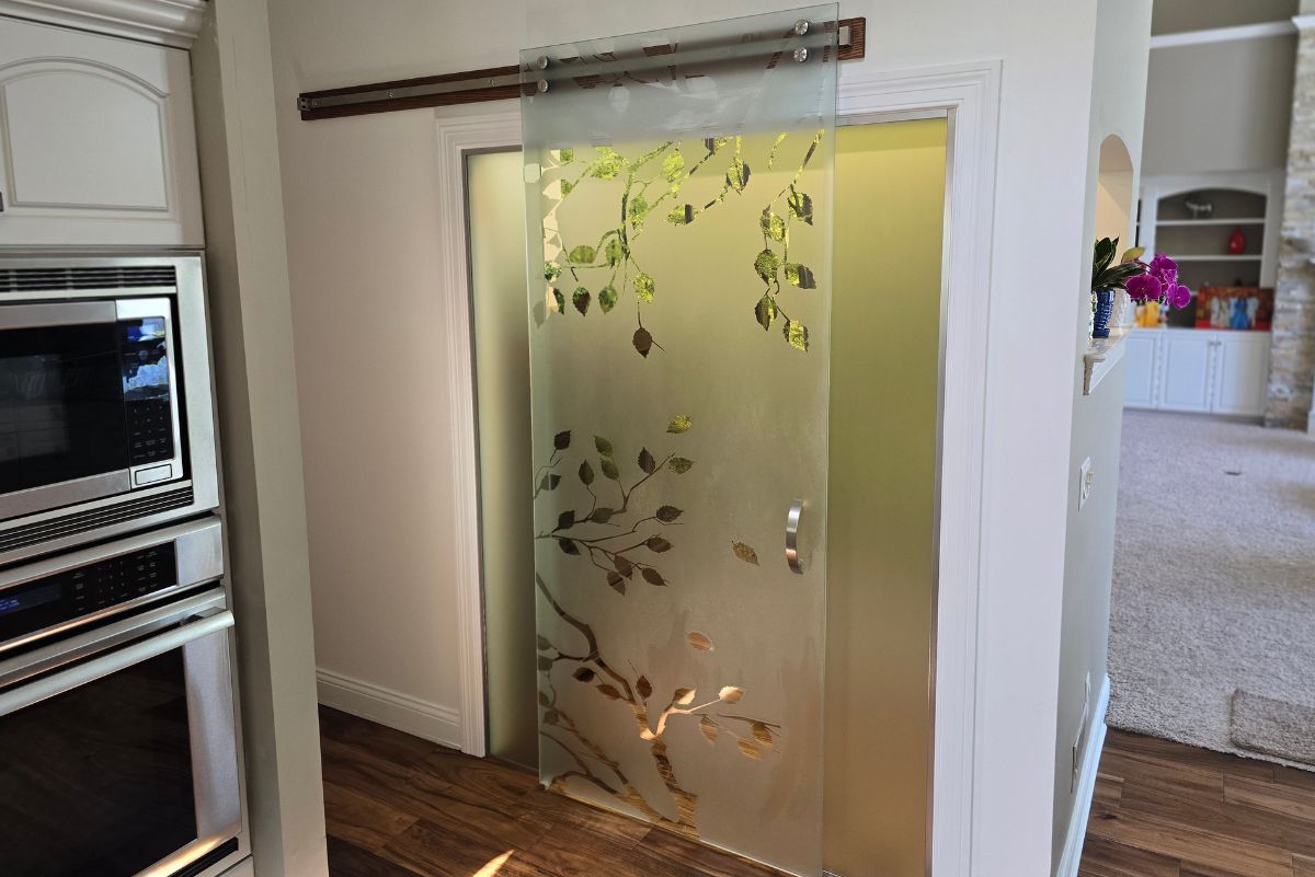 Custom etched decorative glass sliding pantry door installed by RDB Glass in Dayton, Ohio, featuring a detailed artistic leaf design for a modern home interior. Custom etched decorative sliding glass pantry door installed by RDB Glass in Dayton, Ohio, featuring an artistic frosted leaf pattern for upscale residential interiors. decorative glass door Dayton OH, etched glass sliding door, custom pantry glass door, frosted interior door Ohio, artistic glass door design, custom decorative glass Dayton, residential decorative glass, etched leaf pattern glass door