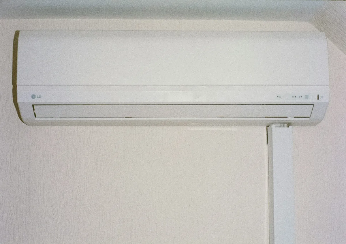 Family relaxing under a wall-mounted AC unit, illustrating the comfort benefits of regular HVAC maintenance in summer.