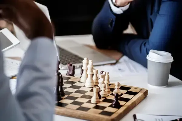 A group of business individuals focused on a chess match at a table, symbolizing strategy and collaboration in decision-making.