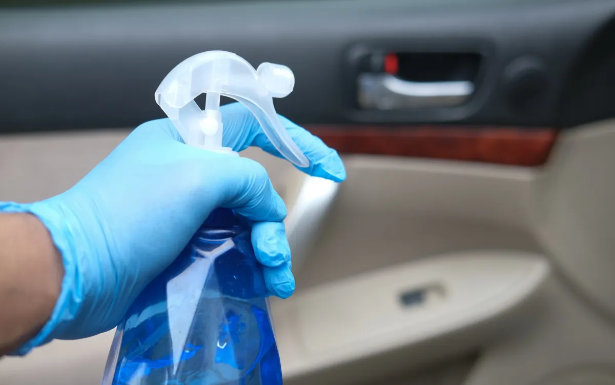 An individual spraying the interior of a car with a cleaning solution