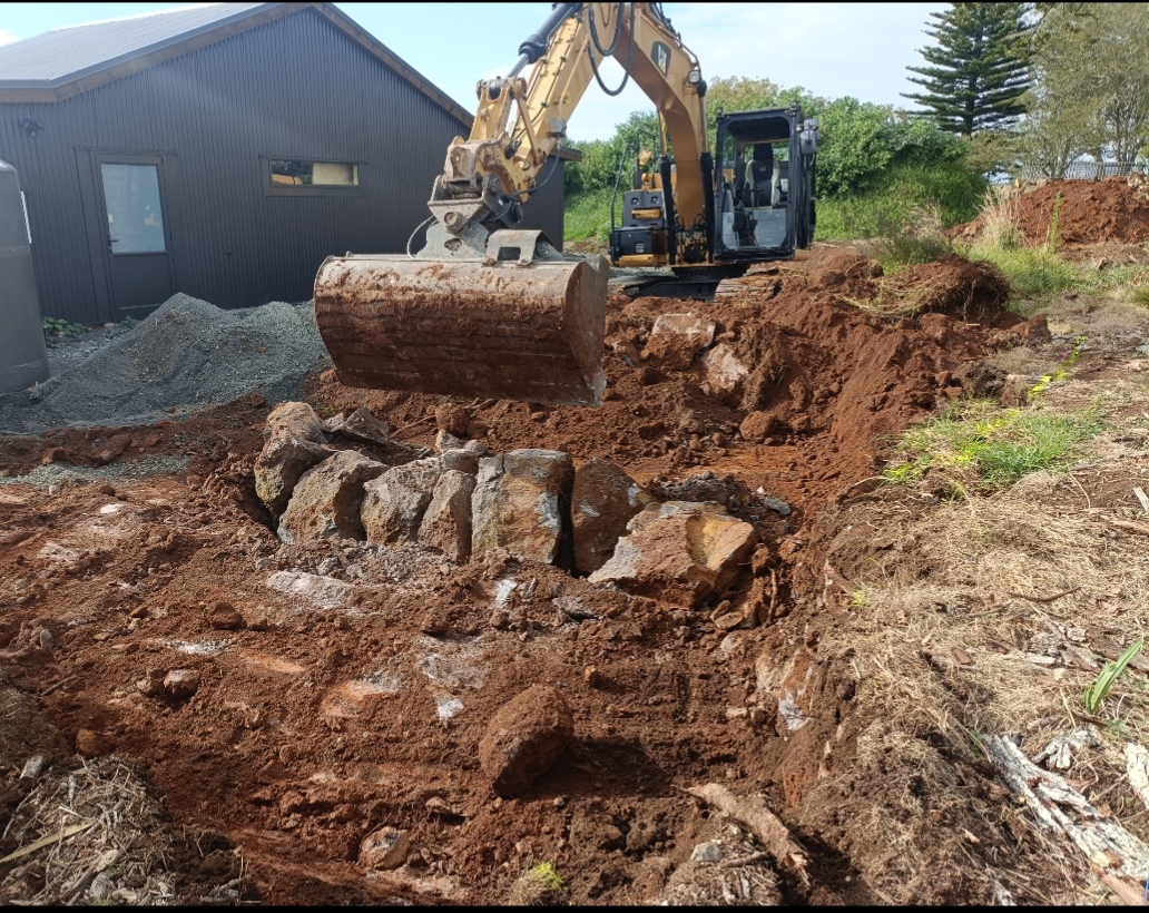 Mini excavator carrying out earthworks and rock removal on rural Northland site