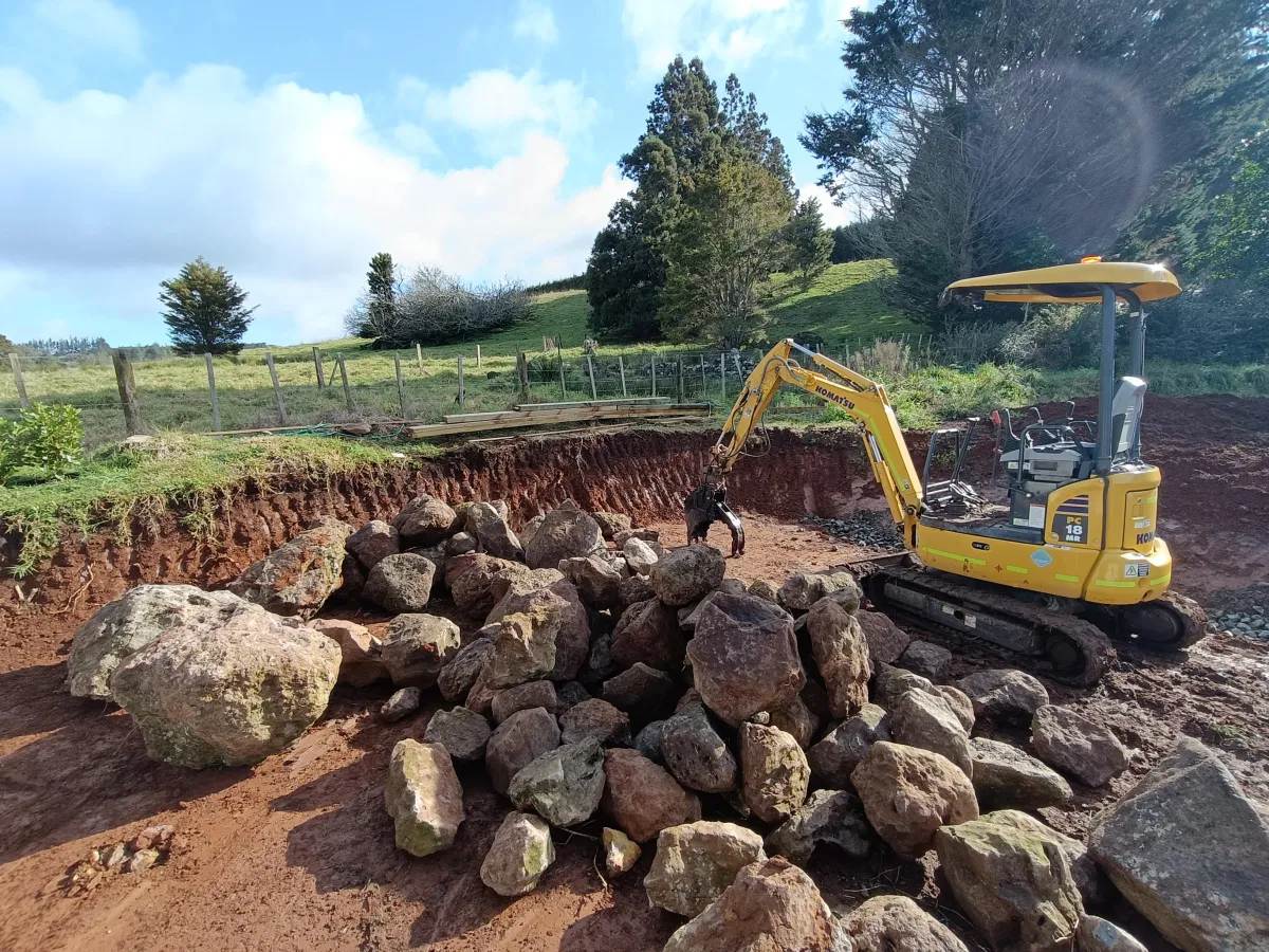 Mini excavator carrying out earthworks and rock removal on rural Northland site