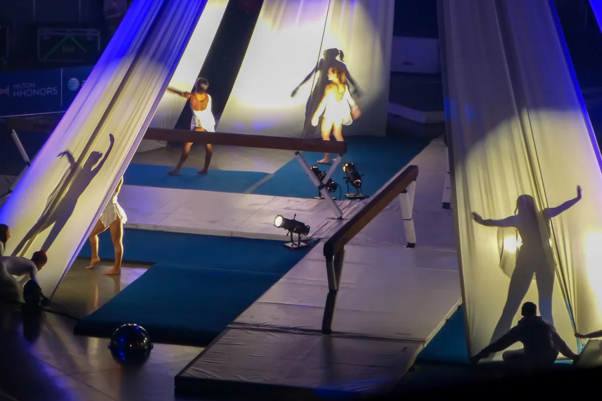 four gymnasts lit up by spotlights with some visible only as shadows and some visible from the back