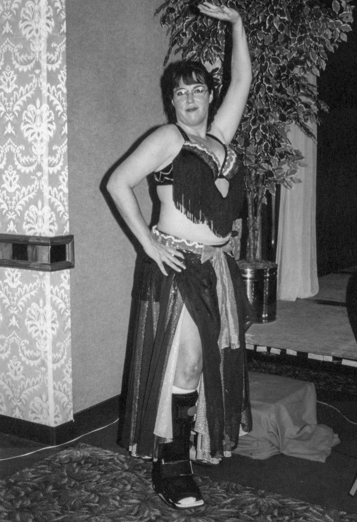 Heather in bellydance costume with one hand on hip and back hand up in the air she also has a cast on her leg