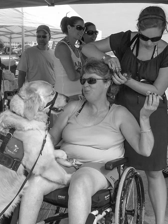 surfing dayHeather sitting on a manual wheelchair in a tank top and shorts with her PCA braiding her hair and Heather's golden retriever service dog has paws on Heather's leg