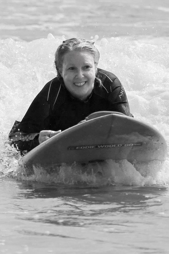 eather wearing a wetsuit laying on a surfboard riding a wave in to the beach