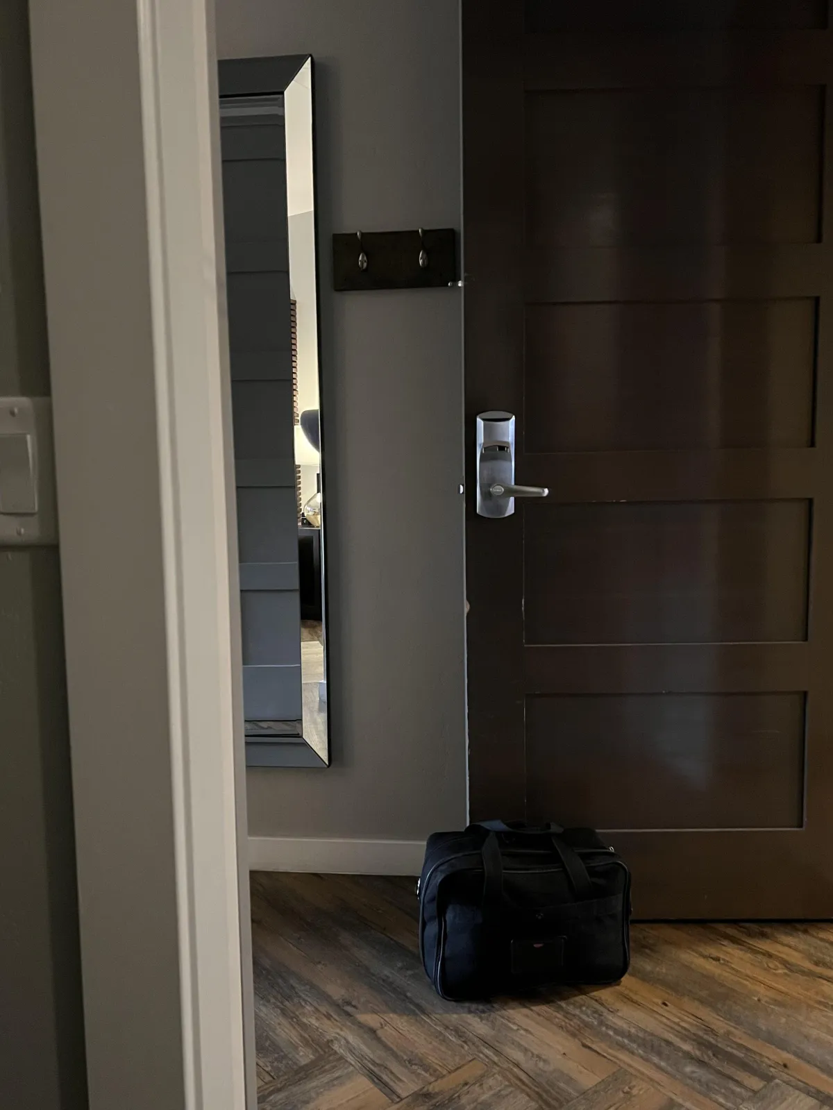 hotel room door propped open by trash can with full-length mirror and coat hooks visible behind the door