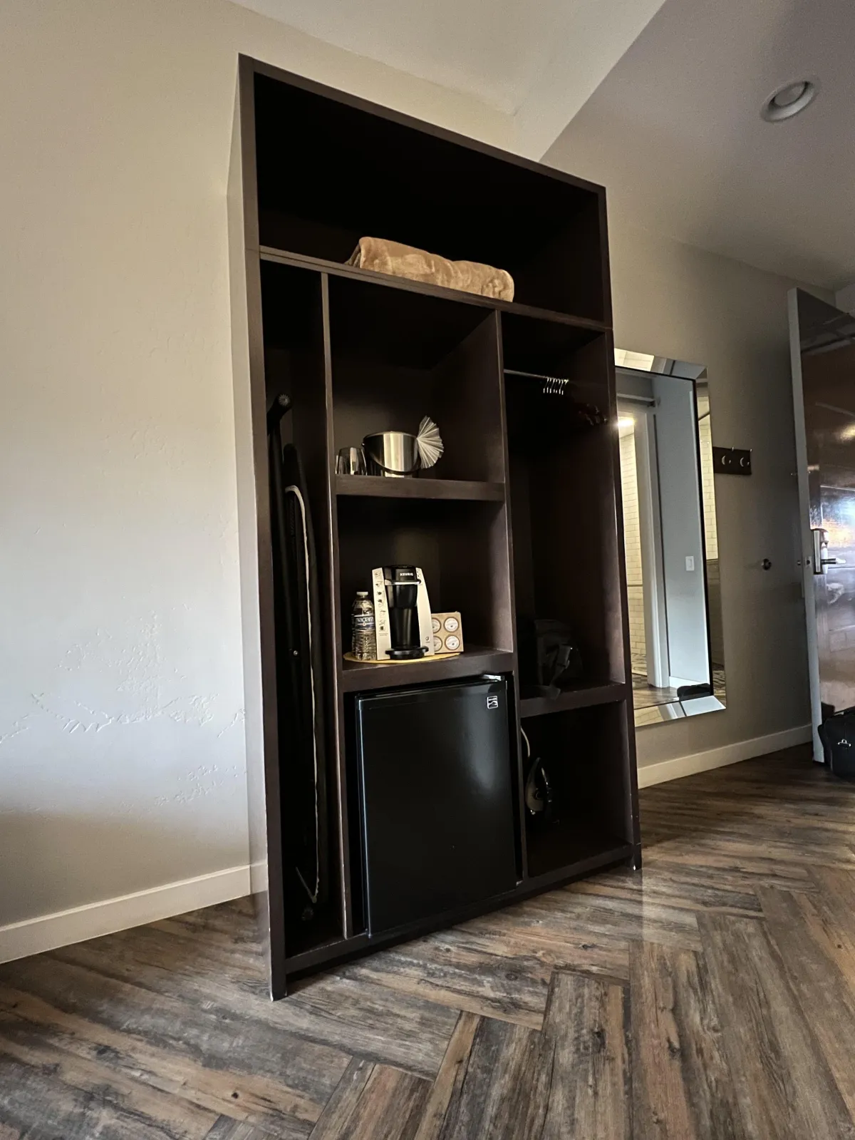 freestanding cabinet with small refridgerator and coffee maker and iron all reachable but the spare blanket is on the topmost shelf