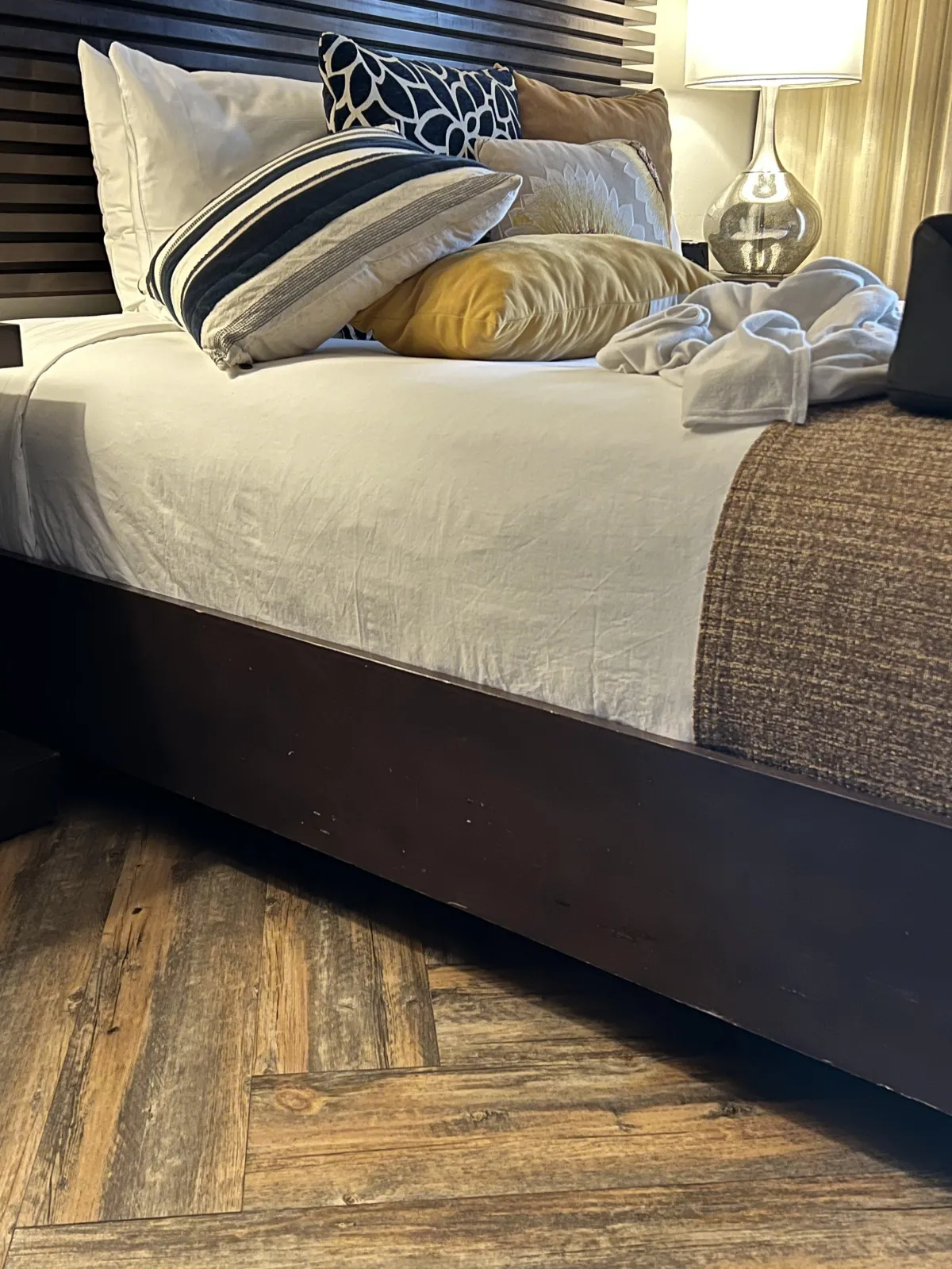 wooden floor with planking in v-pattern and platform bed piled with multiple colored pillows