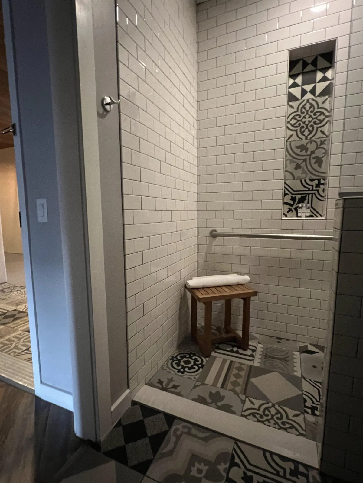 hotel room shower with subway wall tiles and a single horizontal grab bar and a small freestanding teak bench