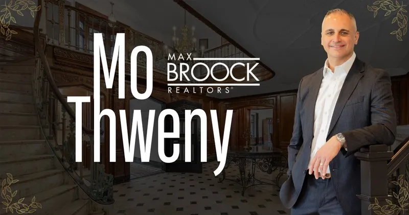 Mo Thweny, real estate agent with Max Broock Realtors, posing in a luxury home foyer with a grand staircase.