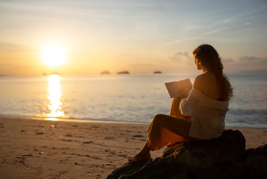 Woman sitting on the beach at sunset, reading a book in quiet reflection