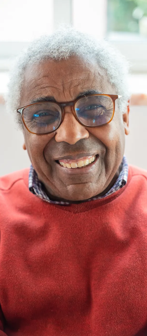 Smiling older man with silver hair wearing a beige henley shirt, standing confidently outdoors with crossed arms.