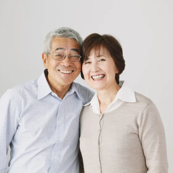 A senior couple standing together in a lush green park, both smiling warmly.