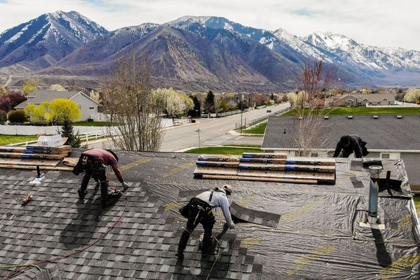 Roof installation crew installing asphalt shingles with mountain backdrop in Utah