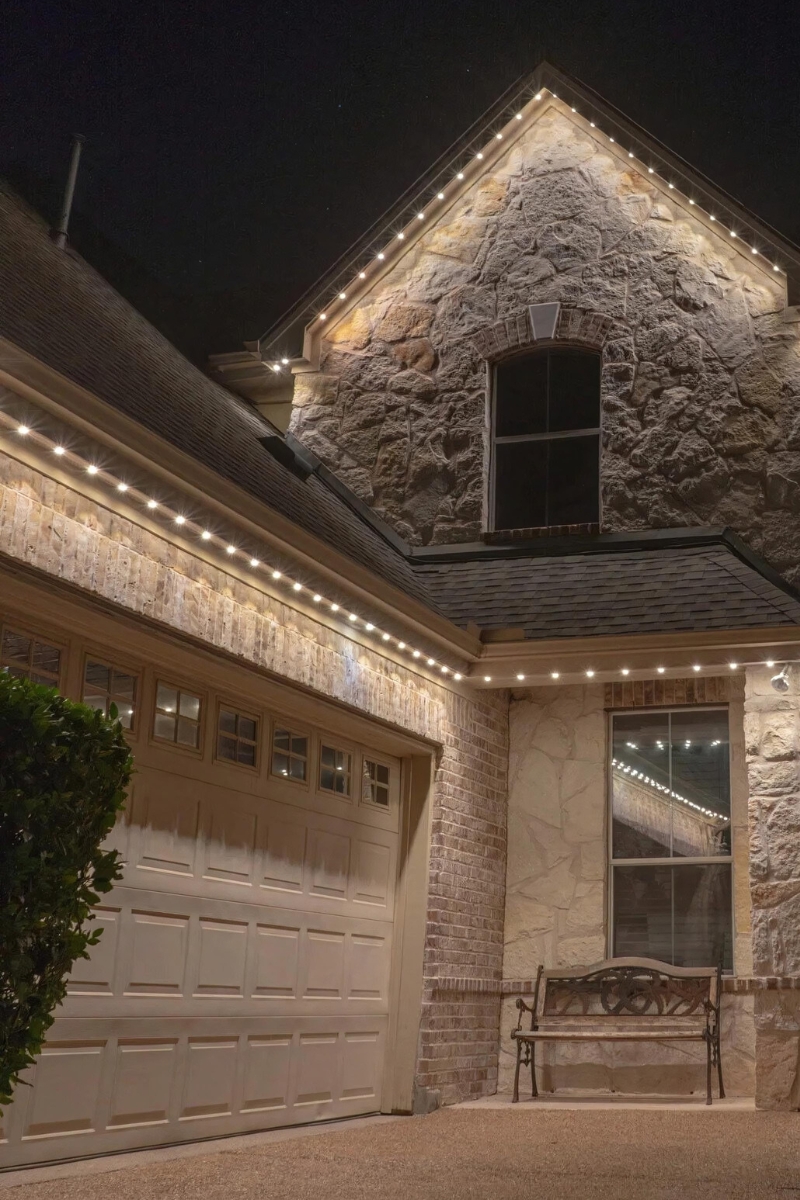 Permanent warm white exterior roofline lighting installed on luxury home in Highland Utah highlighting stone facade and architectural details by PowerHouse Roofing