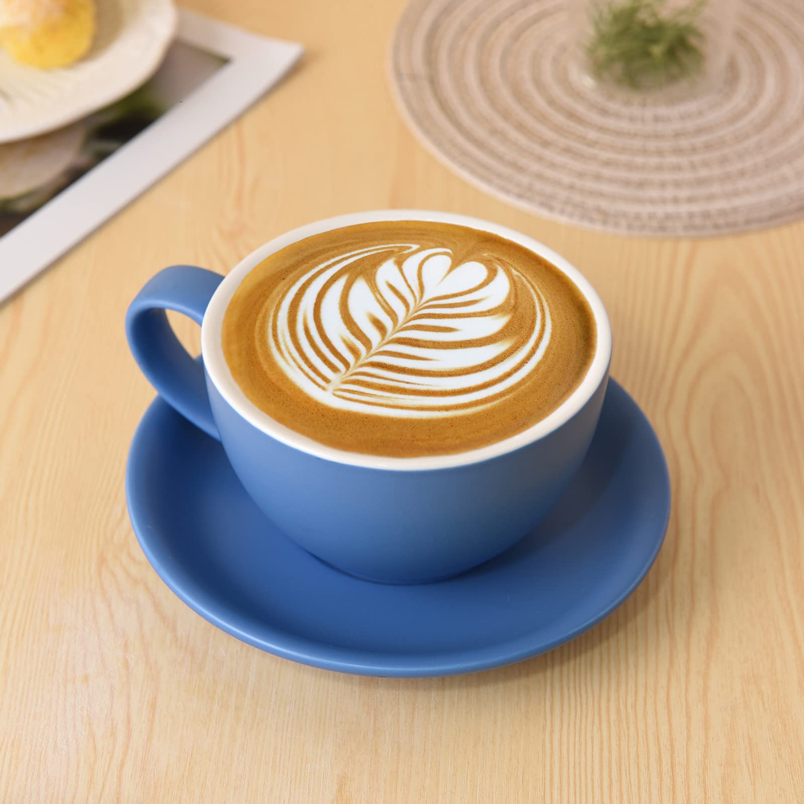 Hot latte with rosetta latte art served in a blue ceramic cup and saucer on a wooden table.