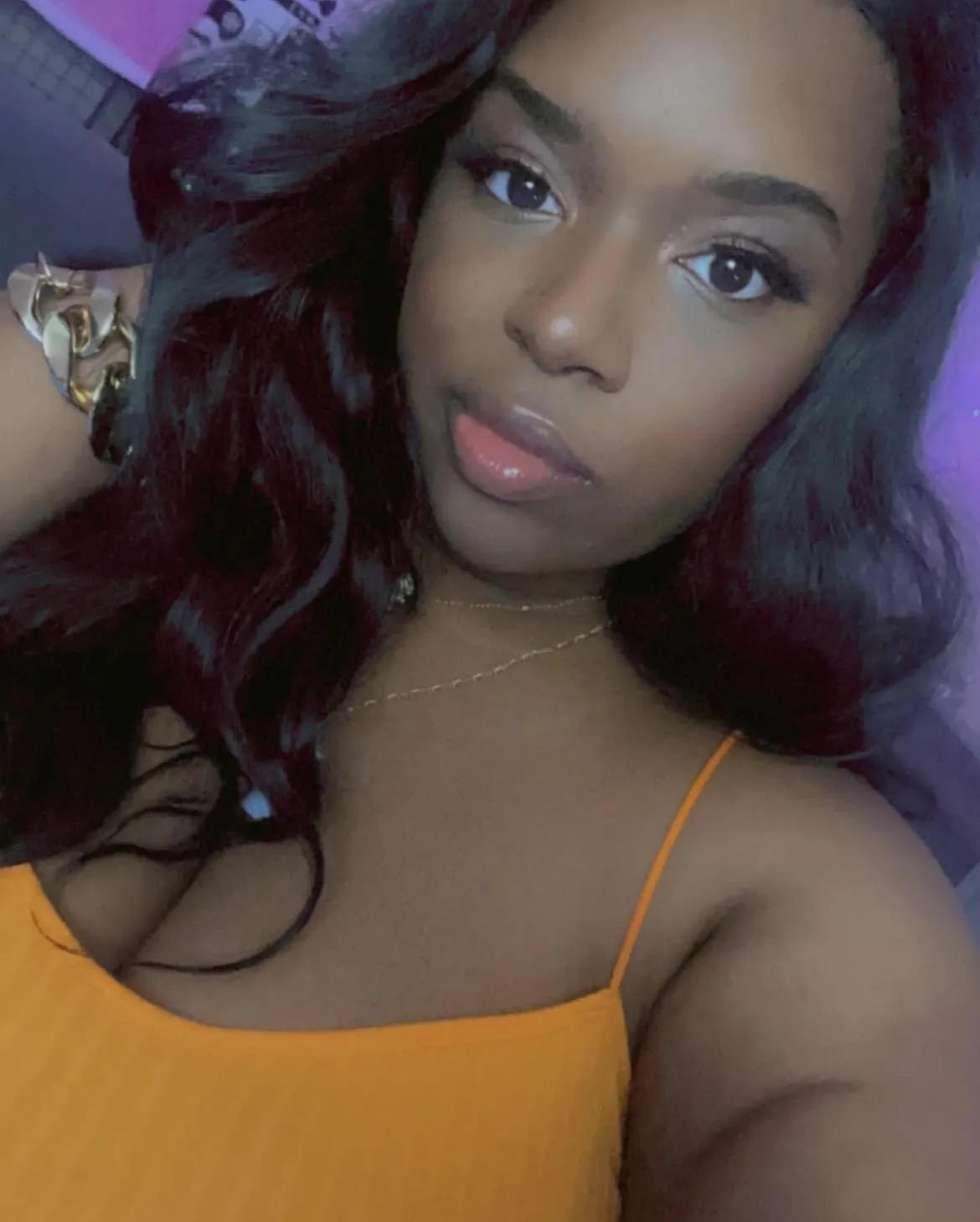 picture of author and founder of Rebranded Nice Girl, she is wearing an orange top, has black wavy hair, golden bracelet, and is smirking