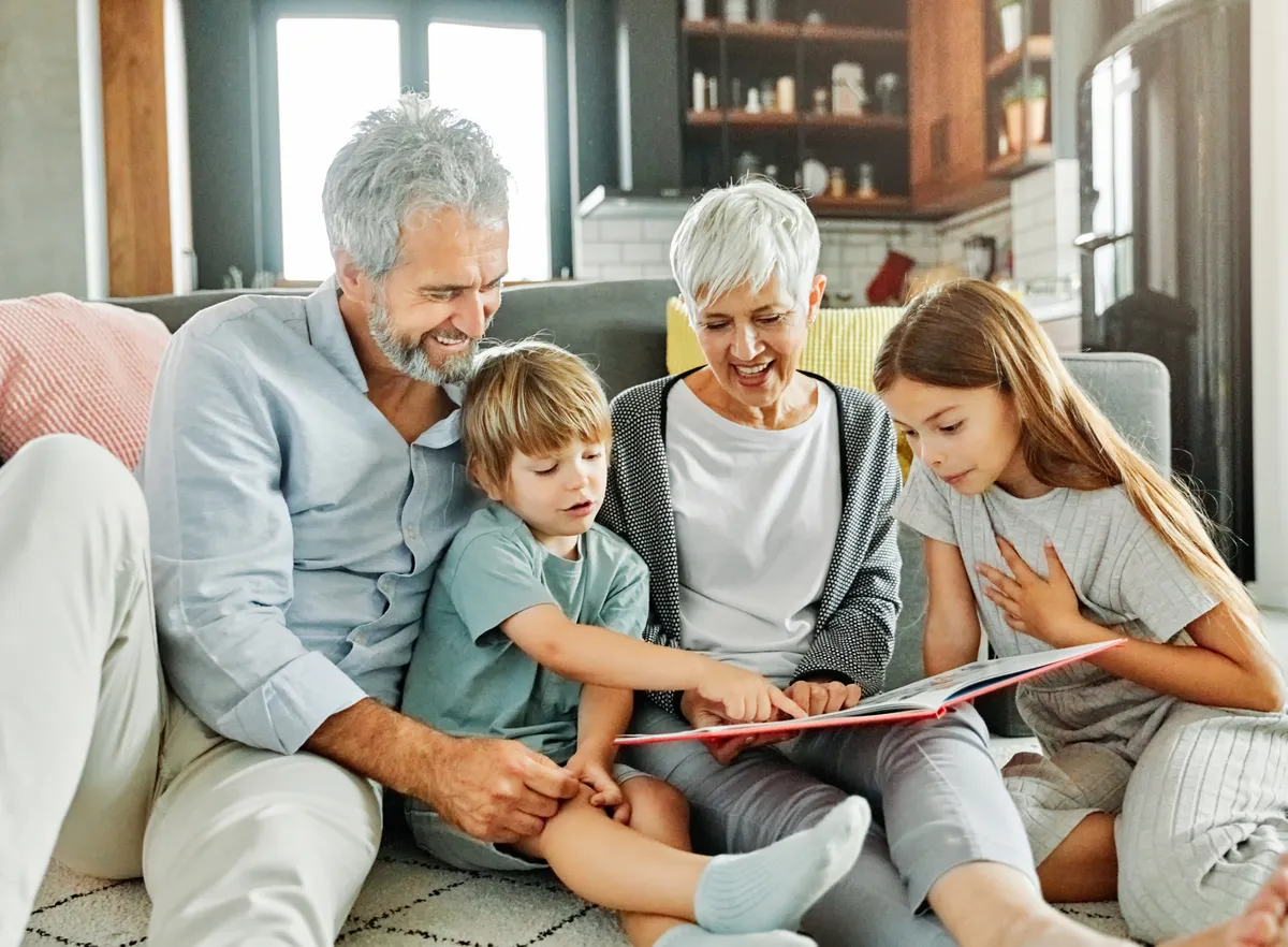 Grandparents reading a book with their two grandchildren on the couch
