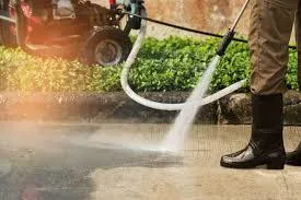 Person using a pressure washer to clean a concrete surface, showcasing effective power washing techniques for exterior maintenance.