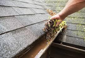 Person removing debris from a clogged gutter, highlighting the importance of gutter cleaning for home maintenance and water damage prevention.