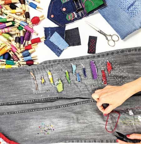 Colourful visible mending on grey jeans with threads and supplies