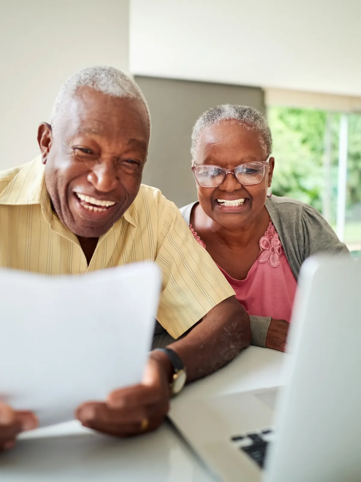 Joyful senior couple with papers using laptop for financial planning, retirement savings.