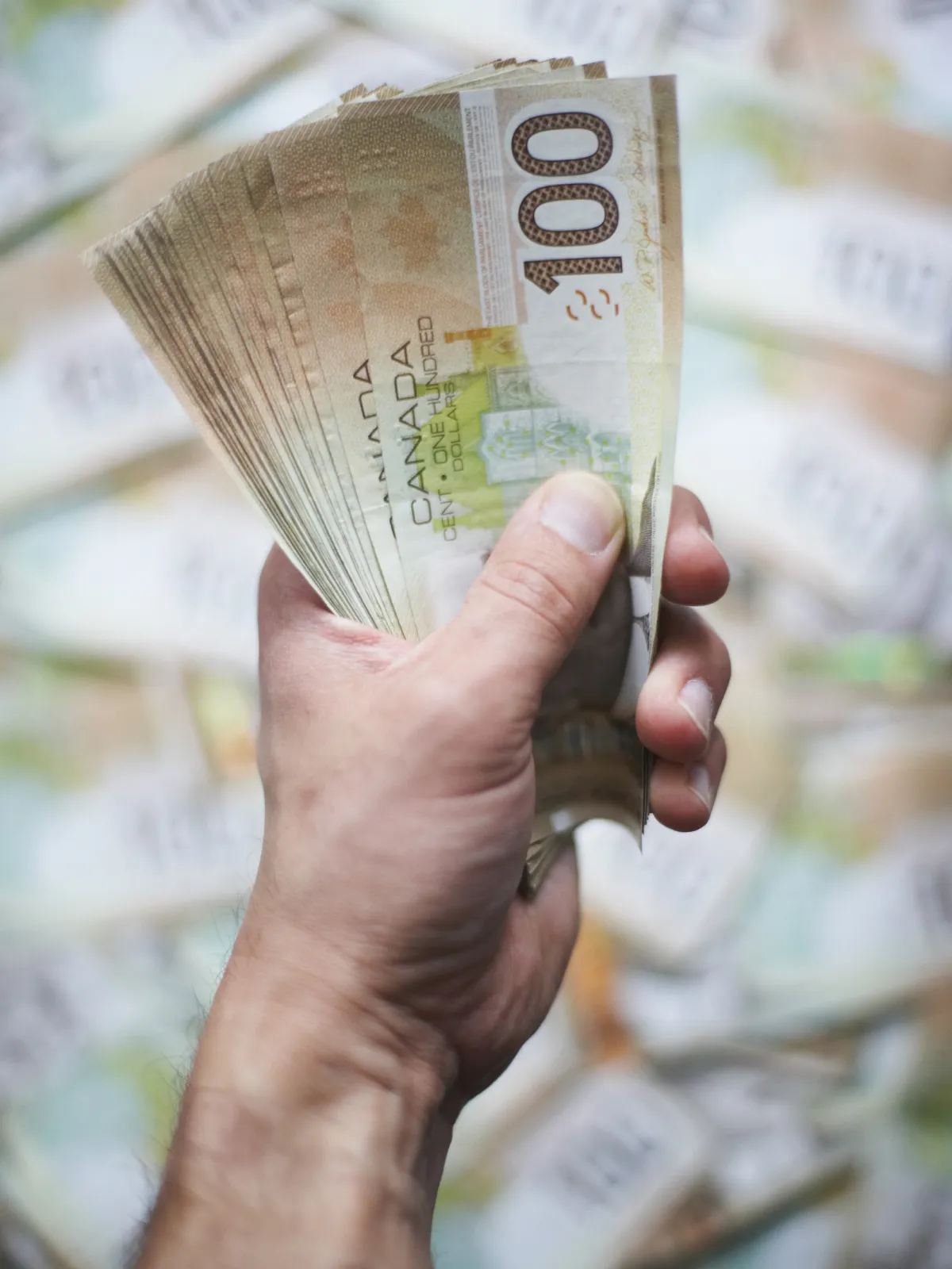 Hand fanning out Canadian $100 bills, wealth, investment earnings.