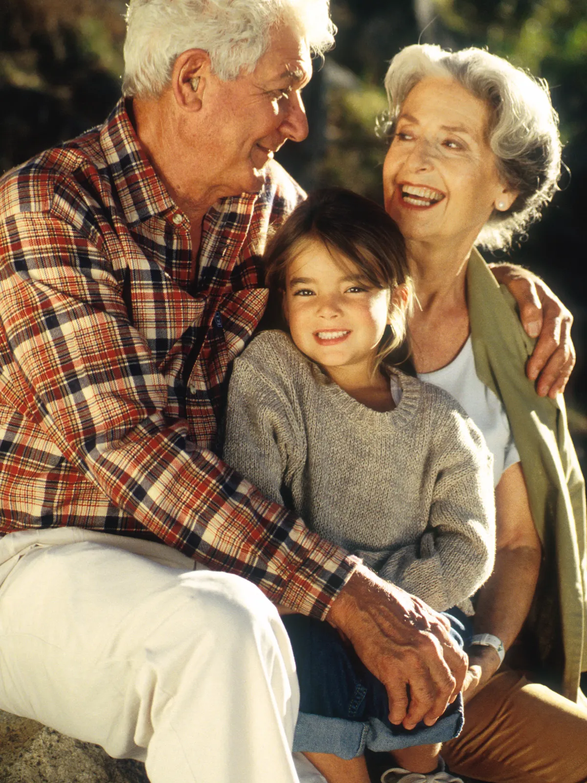 Grandparents with granddaughter smiling outdoors, family, generational bond.