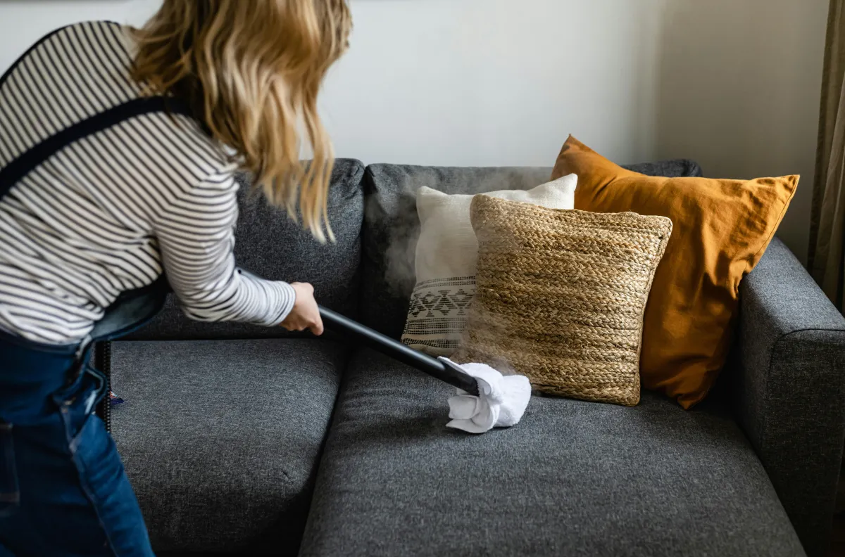 Professional cleaner steam cleaning sofa cushions in residential living room - Rental Turnover and Post-Construction Cleaning - Supreme Sparkle Solutions