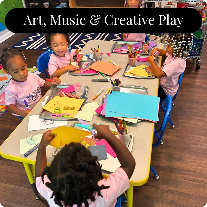 Young children in pink shirts are actively engaged in an art and craft activity at a table with colorful paper and art supplies at Smyrna, GA