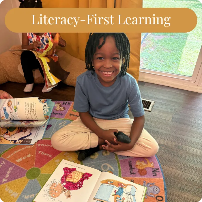 A smiling Black child sits cross-legged on a colorful alphabet rug surrounded by open books at daycare in Smyrna
