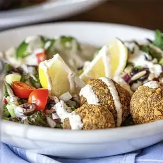 Vegetarian bowl featuring crispy falafel, fresh cucumber salad, and tahini sauce, a healthy choice for appetizer caterings.