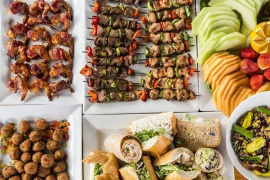Overhead view of diverse buffet platters with kebabs, wraps, and salads by Houston’s stress-free catering solution.