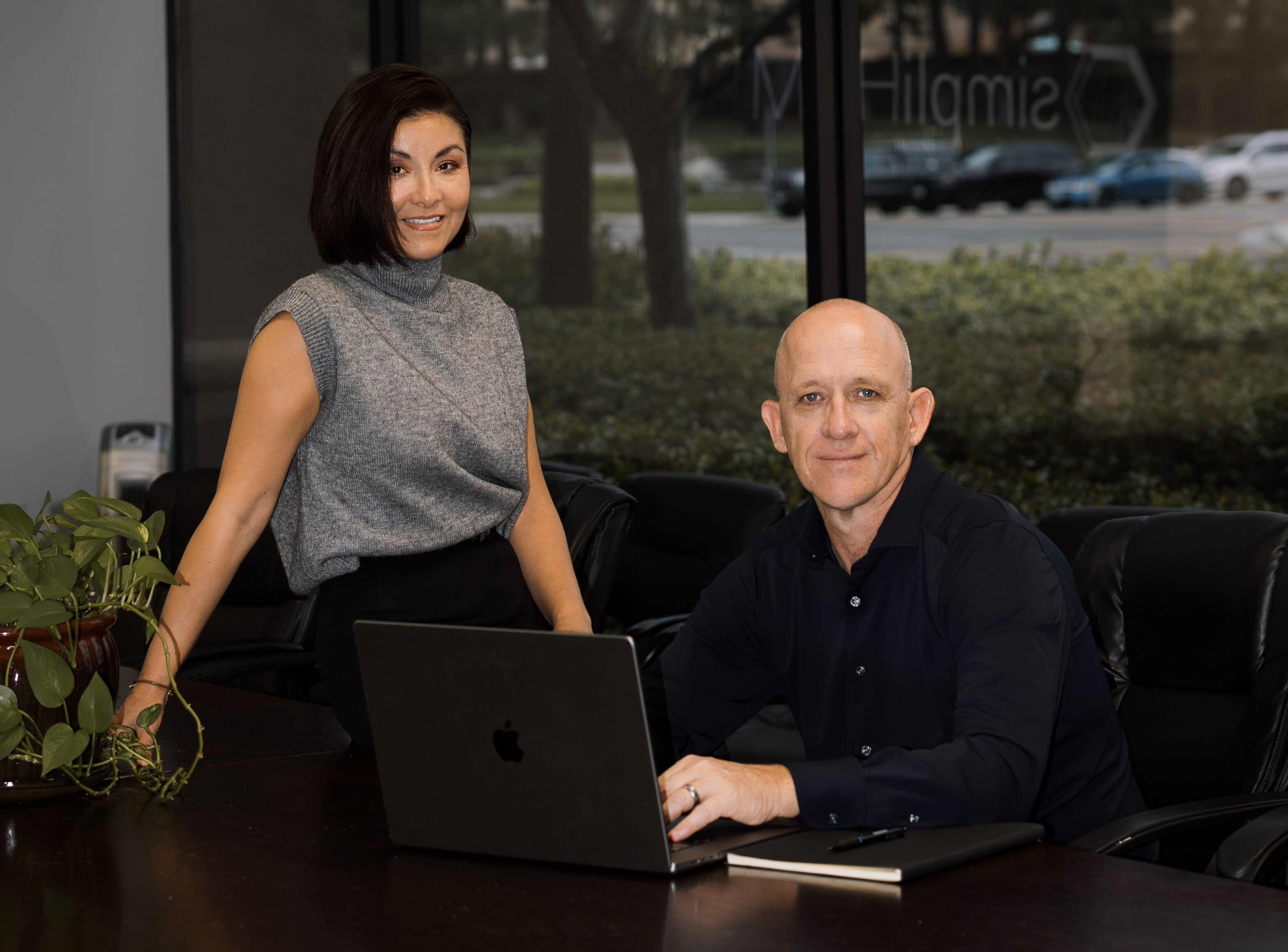 A cheerful young couple sitting at a kitchen island, using a laptop to schedule a real estate consultation. Sunlight streams through a window, highlighting a vase of fresh flowers. The setting is modern and inviting, with a sense of anticipation and excitement.